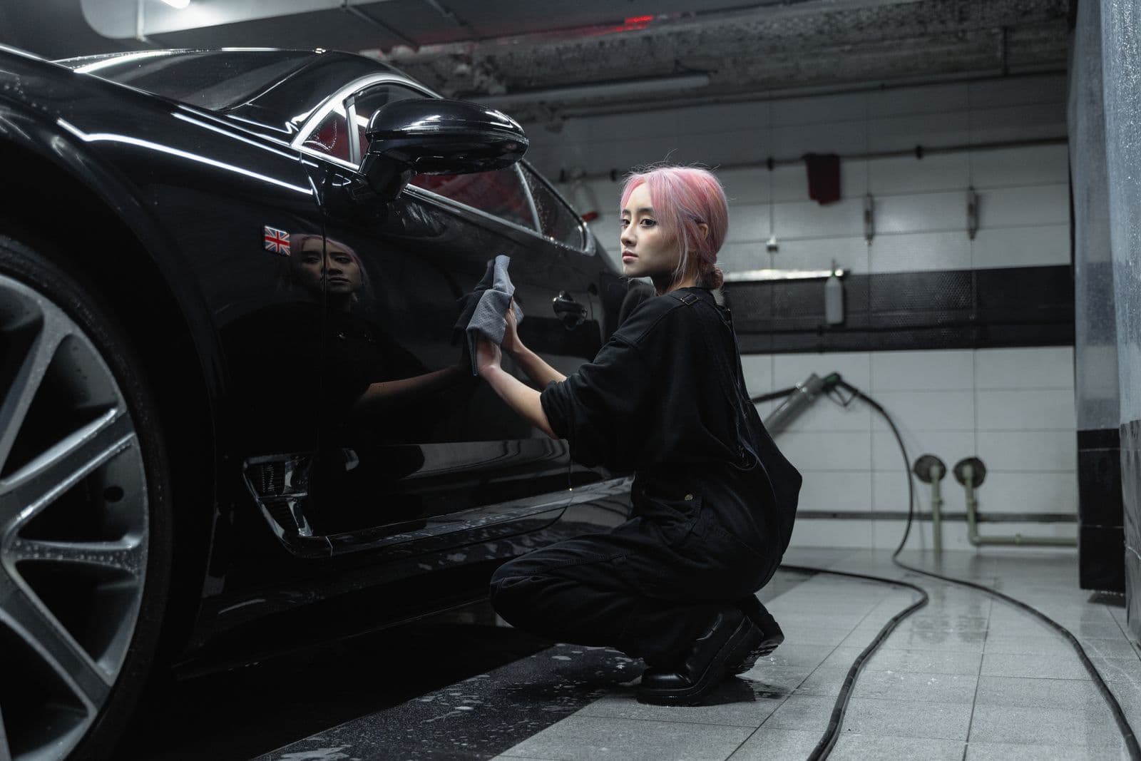 A detailer wiping down a black car in a moody, tiled bay