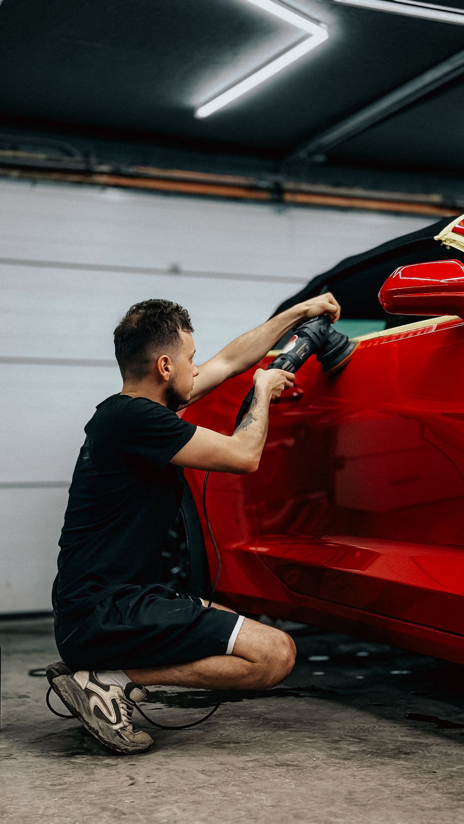 A detailer machine-polishing a red sports car